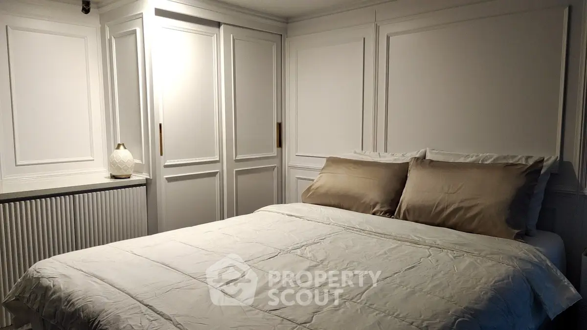Cozy bedroom with elegant white paneling and soft lighting, featuring a comfortable bed and stylish decor.