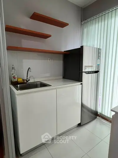 Modern compact kitchen with sleek white cabinets and stainless steel fridge