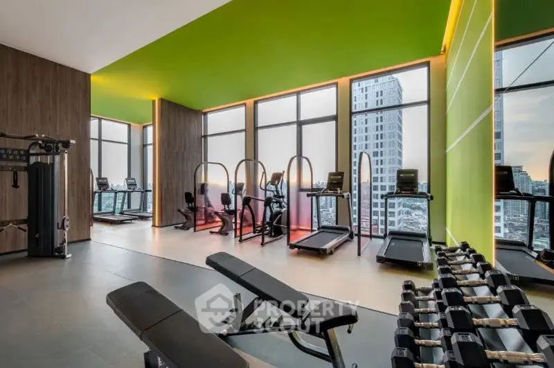 Modern gym with city view, featuring treadmills and weights, in a high-rise building.