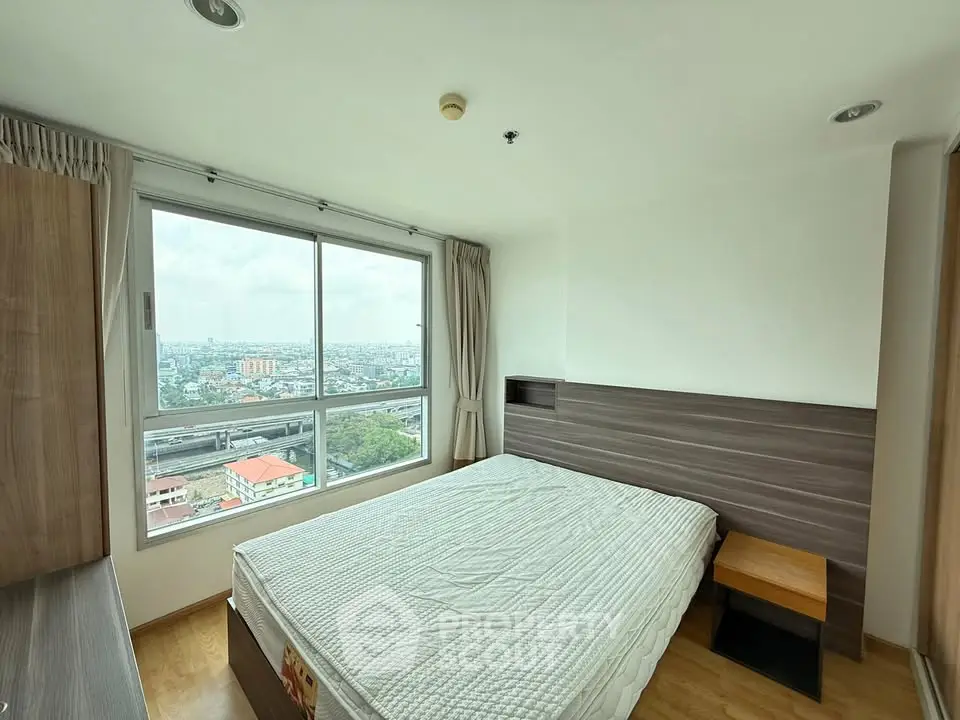 Modern bedroom with large window offering stunning city views, featuring a cozy bed and sleek wooden furnishings.