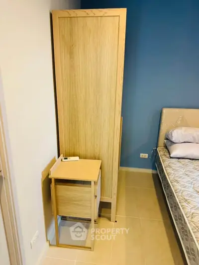 Modern bedroom with wooden wardrobe and bedside table, featuring a comfortable bed and stylish blue accent wall.