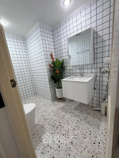Modern bathroom with white tiled walls and terrazzo flooring, featuring a sleek vanity and vibrant plant decor.