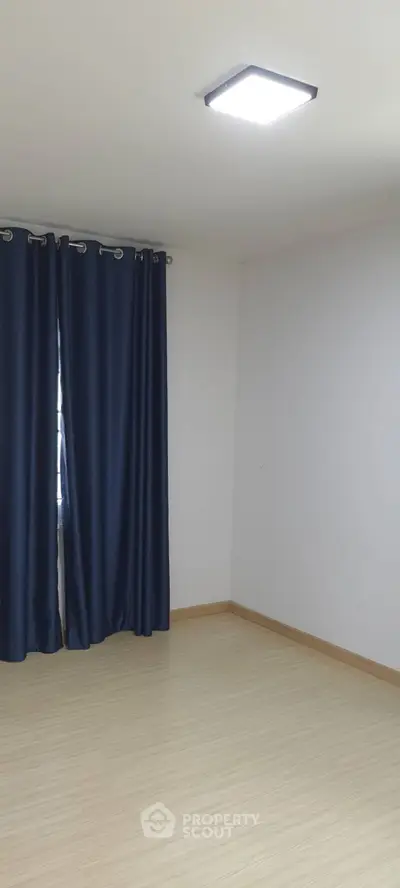 Spacious empty room with wooden flooring and dark curtains, perfect for customization.
