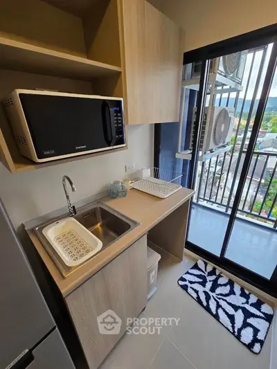 Modern compact kitchen with balcony view, featuring sleek cabinetry and microwave, ideal for urban living.