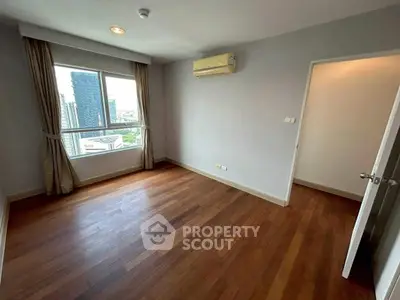 Spacious bedroom with wooden flooring and city view window in modern apartment.