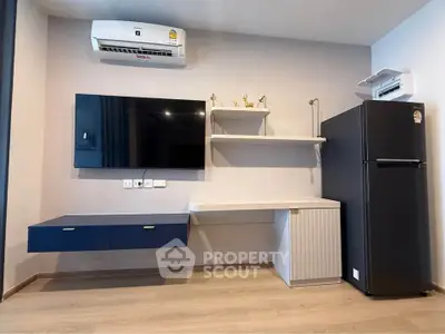 Modern living room with sleek TV setup and air conditioning, featuring a stylish refrigerator and minimalist decor.