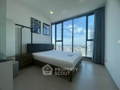 Modern bedroom with floor-to-ceiling windows offering stunning city views, minimalist decor, and ample natural light.
