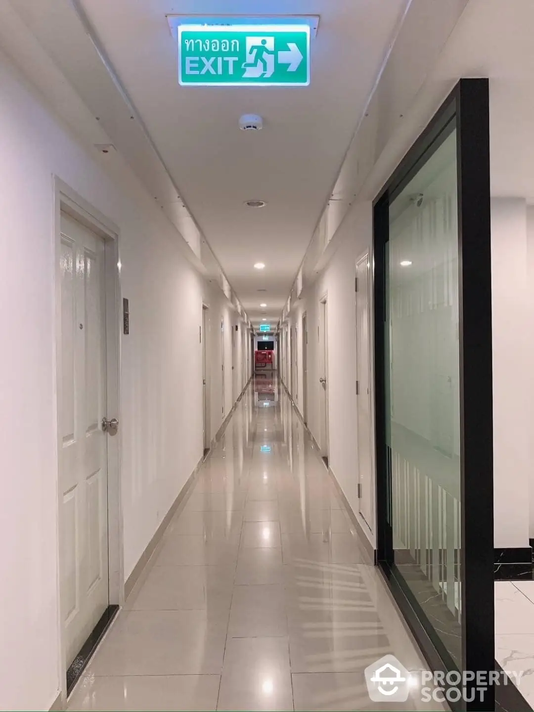 Pristine residential hallway with gleaming tiled floors, modern lighting, and a clear exit sign, offering a welcoming path to luxury living spaces.