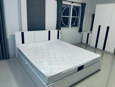 Modern minimalist bedroom with sleek white furniture and large window.