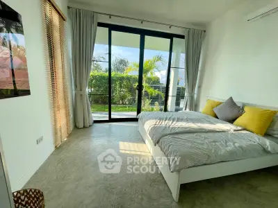 Bright bedroom with large glass doors opening to a lush garden view, featuring modern decor and cozy bedding.
