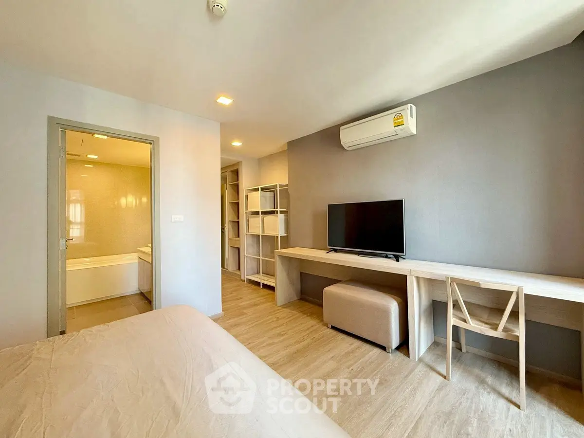 Modern bedroom with TV, air conditioning, and ensuite bathroom in stylish apartment.