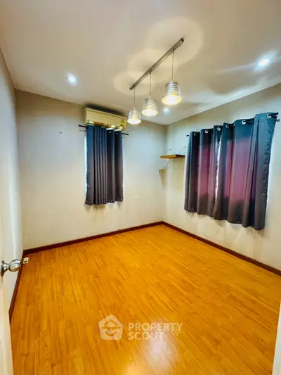 Spacious empty room with wooden flooring and modern lighting