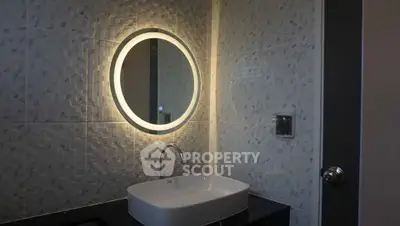 Modern bathroom with illuminated round mirror and sleek sink design.