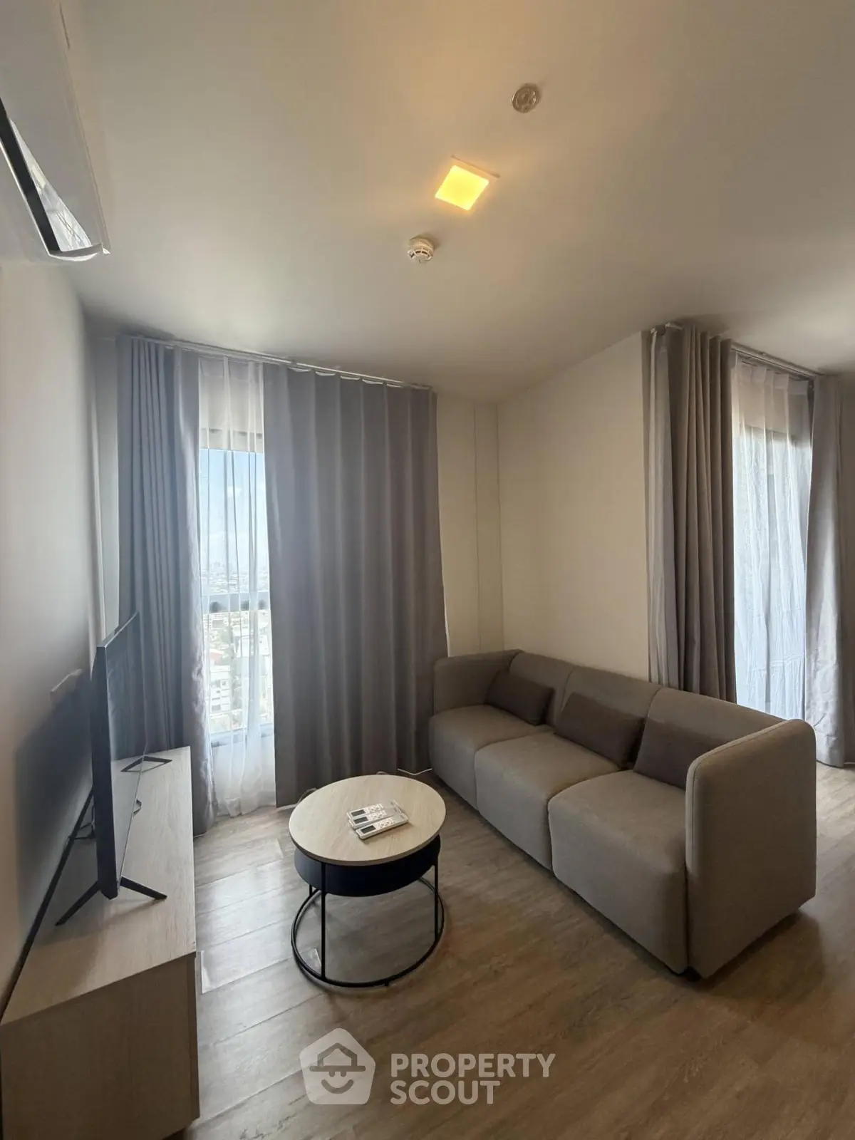 Modern living room with sleek sofa and large windows offering natural light and city views.