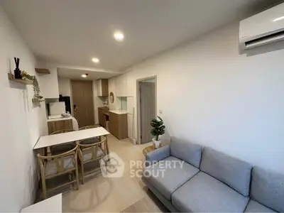 Modern living room with cozy gray sofa, dining area, and compact kitchen in open layout apartment.