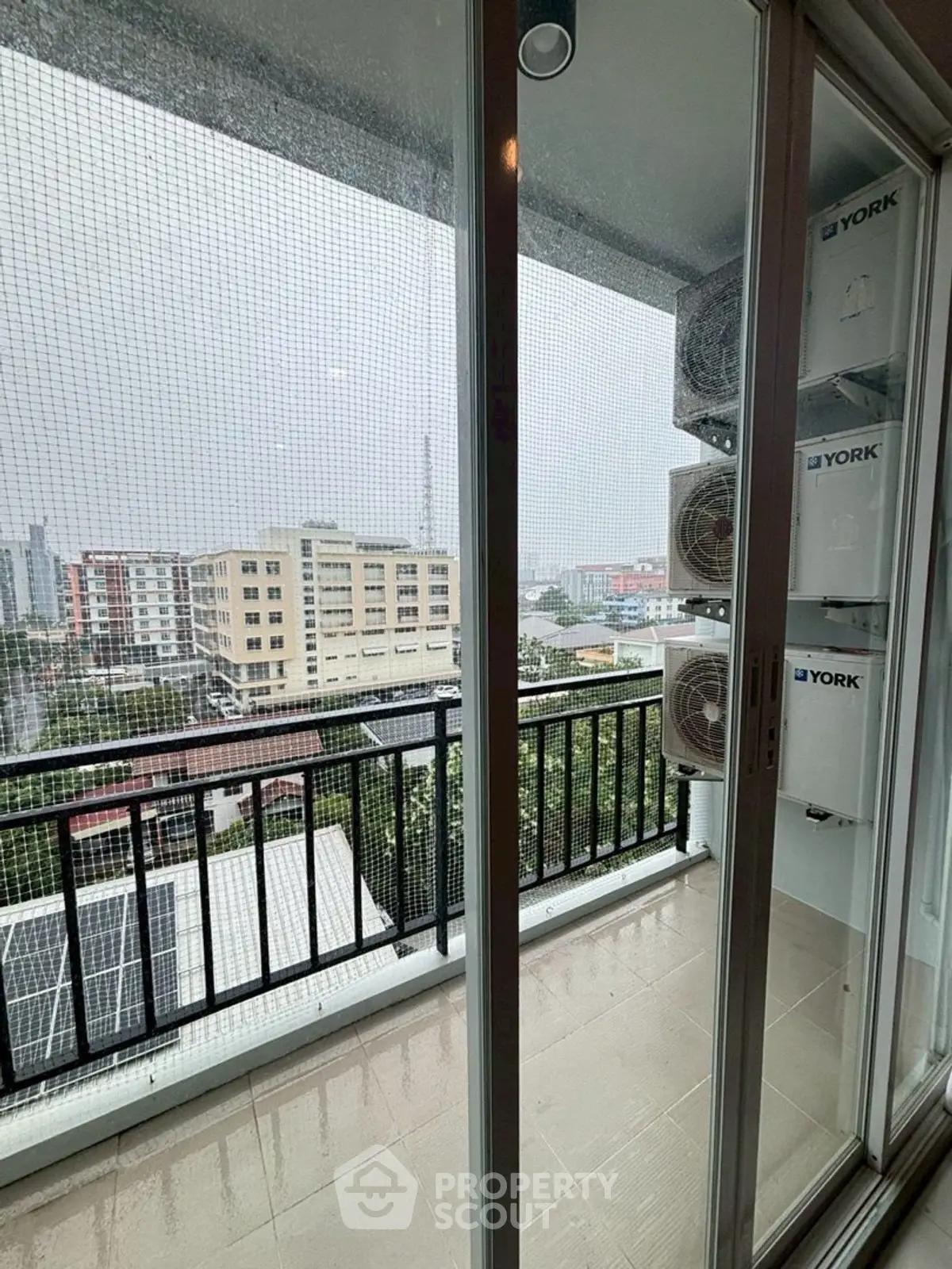Modern balcony with city view and air conditioning units on a rainy day.