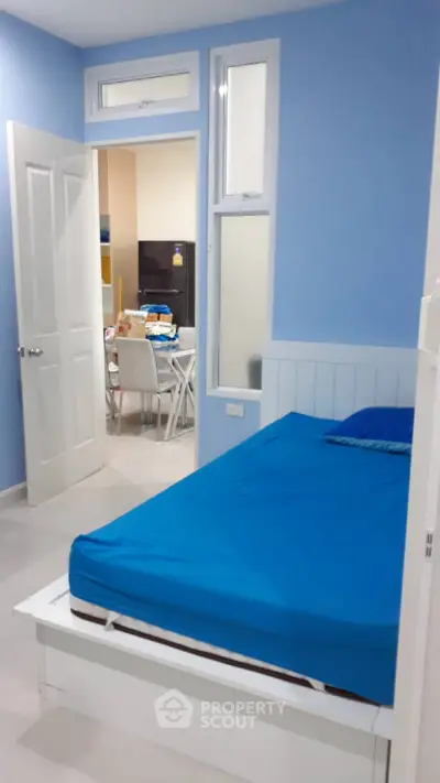Cozy bedroom with blue walls and bed, open door to dining area