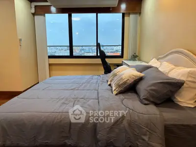 Spacious bedroom with large window offering stunning city view, cozy bedding, and elegant decor.