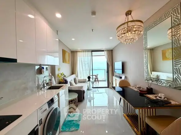Luxurious open-plan living room with ocean view, elegant chandelier, and modern kitchen appliances.