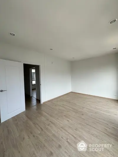 Spacious empty room with wooden flooring and white walls, ideal for customization.