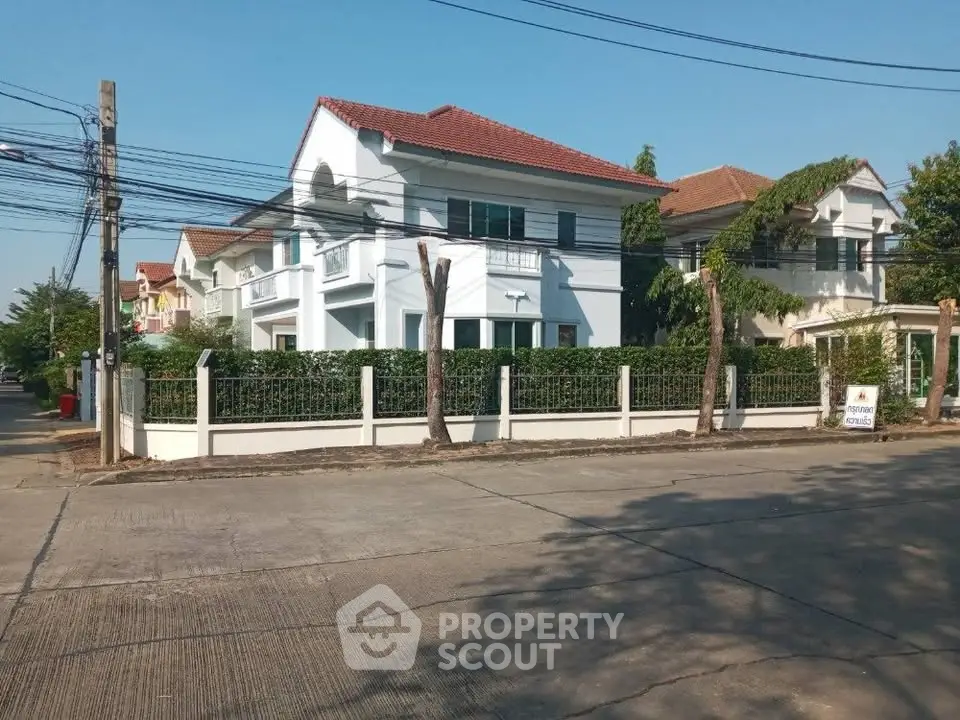 Charming two-story house with red roof and lush greenery in a serene neighborhood.