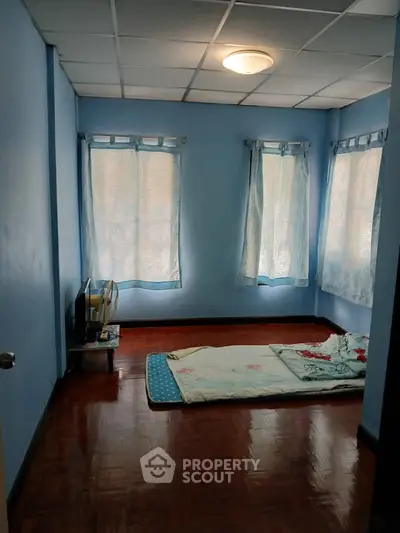 Cozy minimalist bedroom with blue walls and natural light from multiple windows.