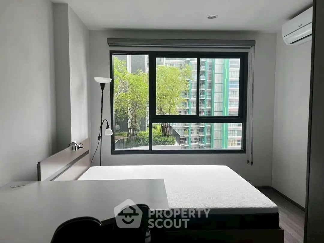 Modern bedroom with large window and city view, featuring minimalist decor and natural light.