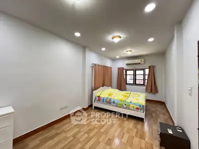 Spacious bedroom with wooden flooring and natural light, featuring a cozy bed and modern lighting.