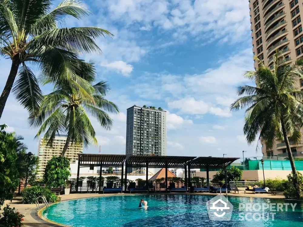 Luxurious poolside view with palm trees and high-rise buildings under a clear blue sky.