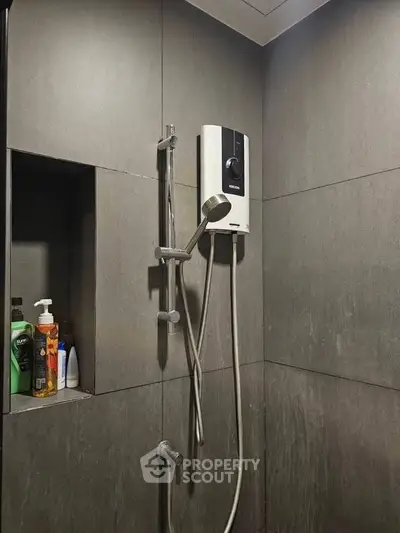 Modern bathroom shower area with sleek gray tiles and built-in shelf for toiletries.