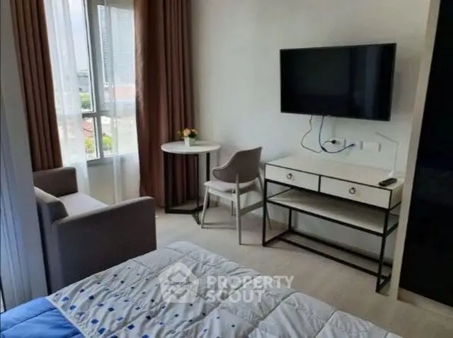 Cozy bedroom with modern decor, featuring a wall-mounted TV and a small seating area by the window.