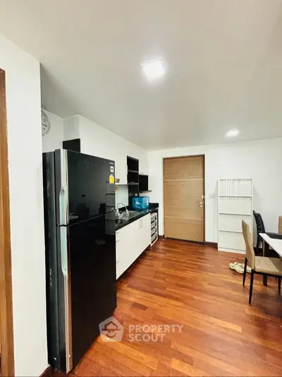 Modern kitchen with sleek black fridge and wooden flooring in a cozy apartment.