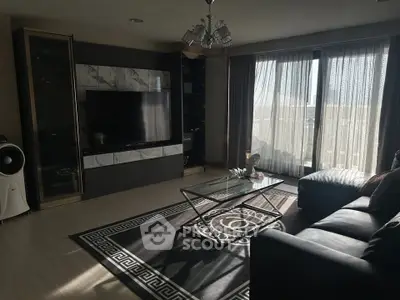 Modern living room with large TV, stylish furniture, and natural light from floor-to-ceiling windows.