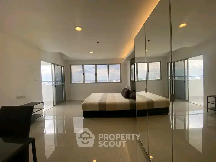 Spacious modern bedroom with large windows and mirrored wardrobe in a high-rise apartment.