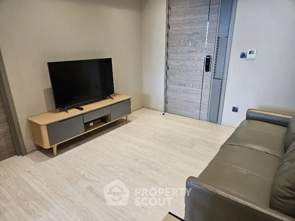Modern living room with sleek furniture and flat-screen TV, featuring light wood flooring and neutral tones.