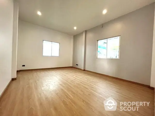 Spacious and well-lit empty living room with polished wooden floors and multiple windows offering natural light, ideal for customization.