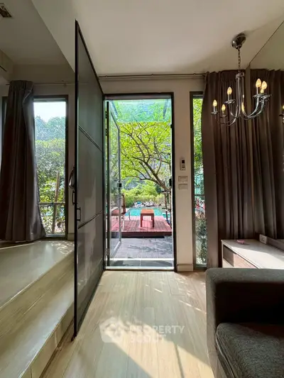 Charming living room with open door to lush garden and elegant chandelier lighting.