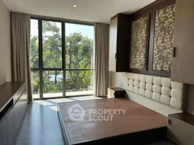 Spacious bedroom with large windows and elegant decor overlooking lush greenery.