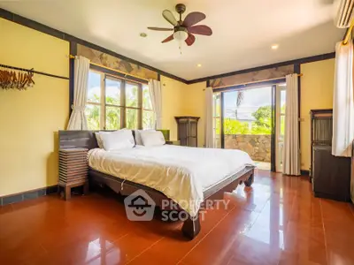 Spacious bedroom with large windows and garden view, featuring elegant wooden furniture and ceiling fan.