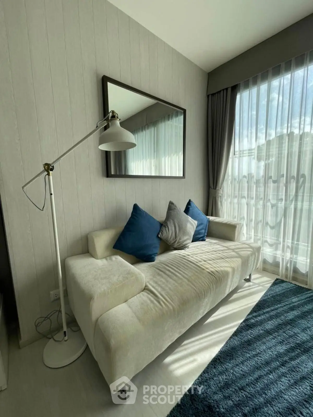 Modern living room with stylish sofa and floor lamp, featuring large window with natural light.