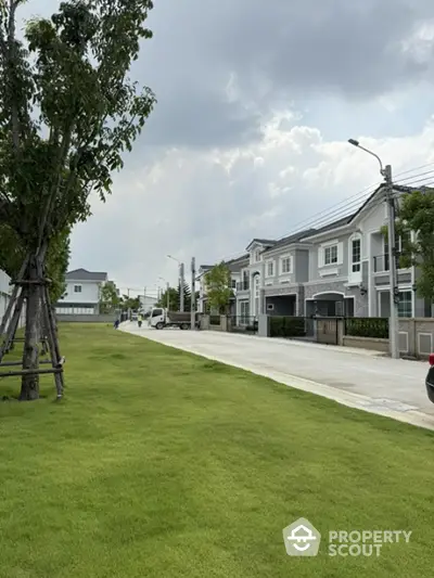 Charming suburban neighborhood with modern townhouses and lush green lawns under a cloudy sky.