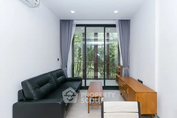 Modern living room with sleek black sofa and large glass doors opening to a lush garden view.