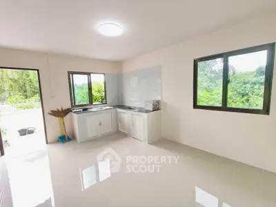 Bright kitchen with large windows and scenic greenery view, featuring sleek white cabinetry and tiled flooring.