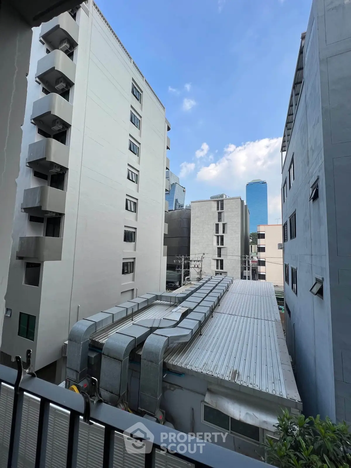 Urban view from balcony showcasing cityscape and modern buildings under blue sky.