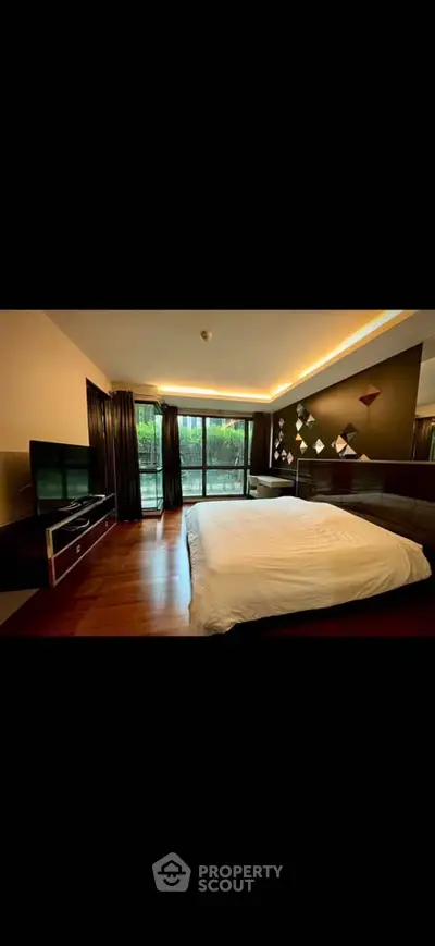 Luxurious bedroom with modern decor and large windows overlooking greenery, featuring elegant lighting and hardwood floors.
