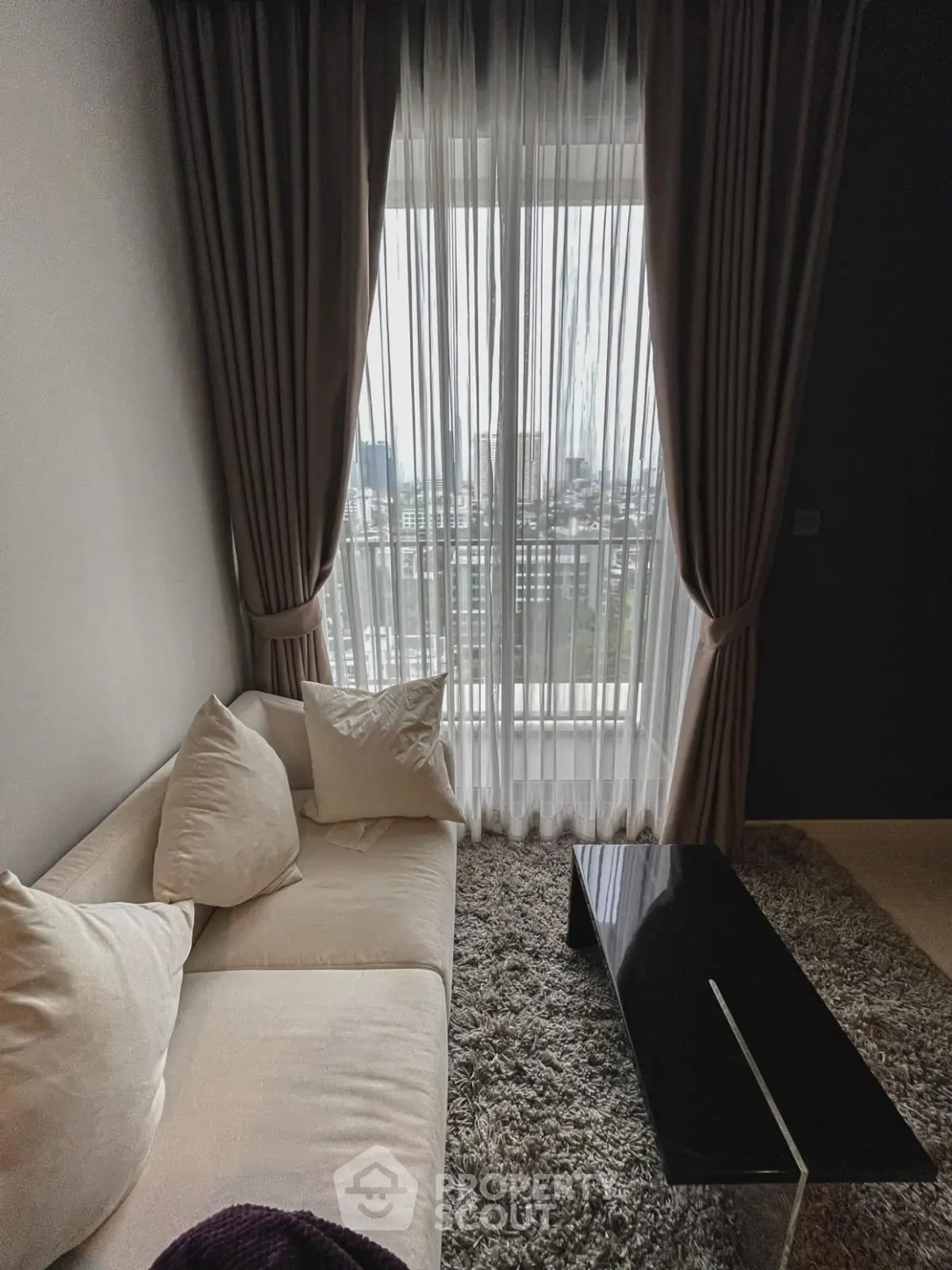 Cozy living room with city view, featuring a plush sofa and elegant curtains.