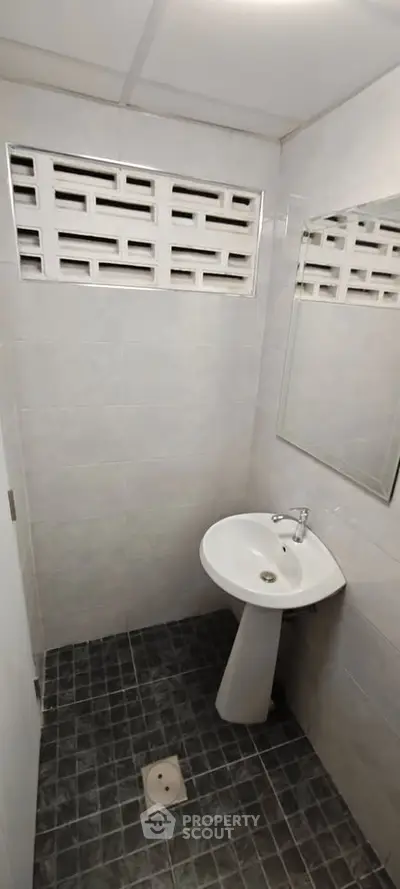 Compact bathroom with pedestal sink and tiled walls, ideal for small spaces.