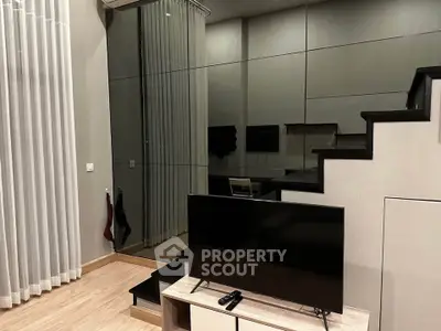 Modern living room with sleek TV setup and mirrored wall under staircase