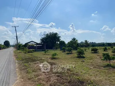 Expansive land plot with clear skies, ideal for development or agriculture, featuring a rural road and lush greenery.