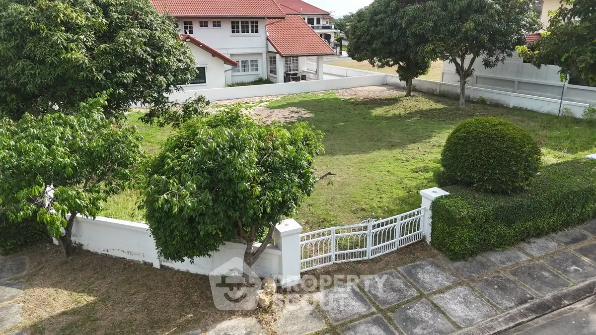 Spacious residential plot with lush greenery and charming red-roofed houses in a serene neighborhood.